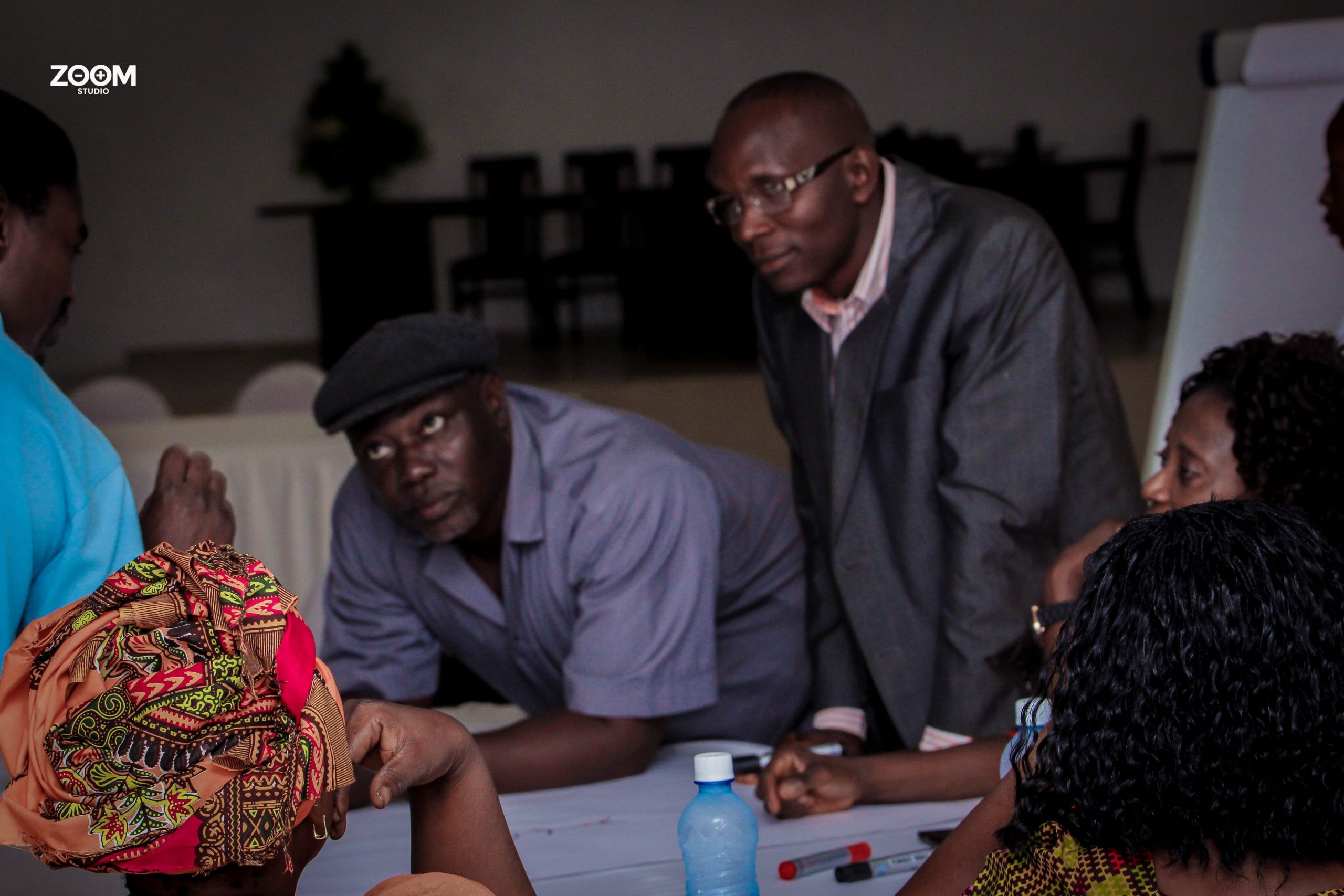 Two standing African men in shirts and suits listen intently to someone off camera