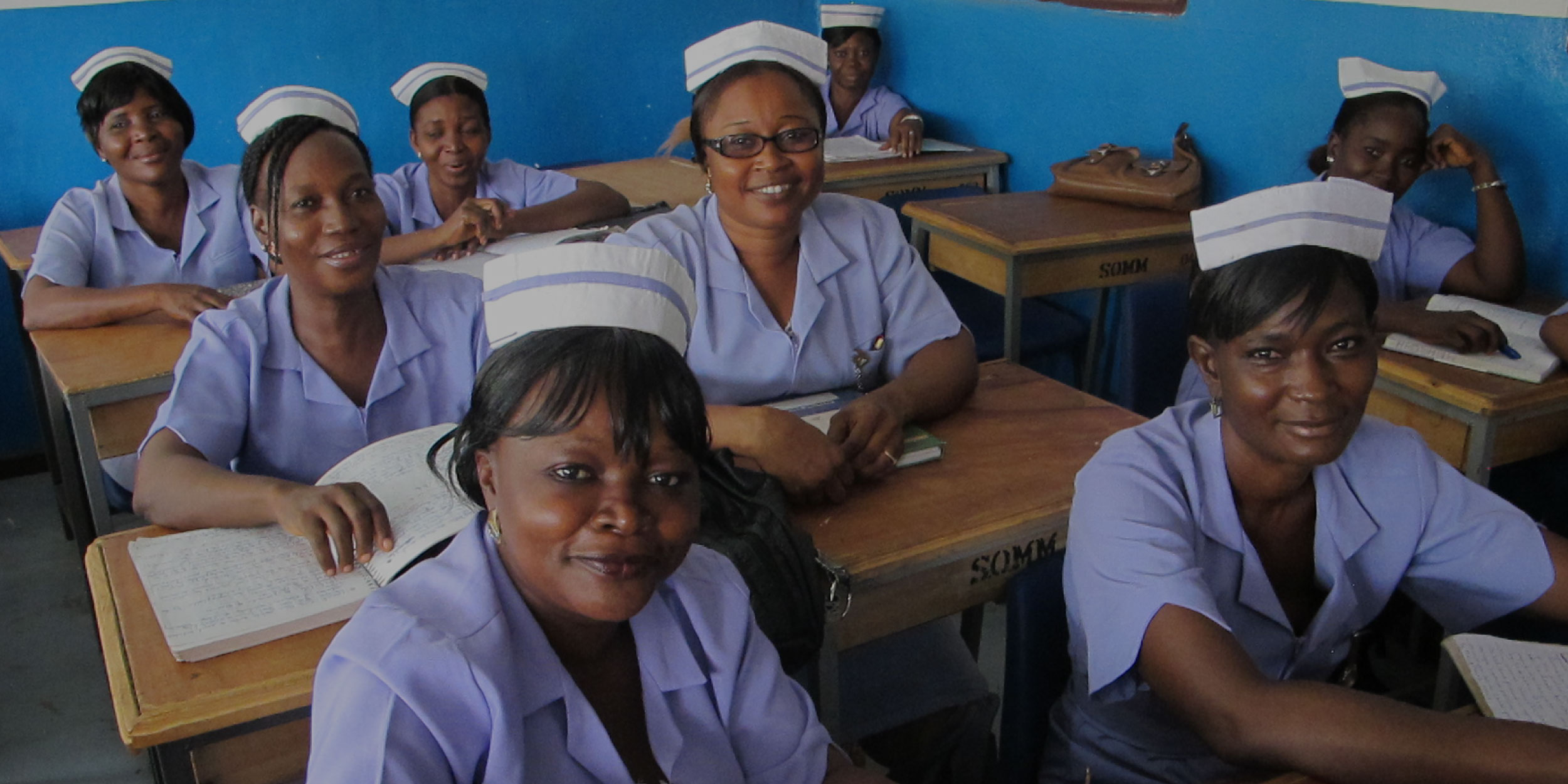A group of seated African female nurses in uniform, smiling at the camera